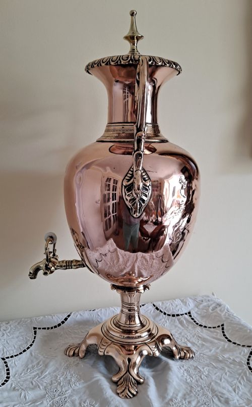 fig 1. A polished copper and brass Victorian tea urn featuring twin side scroll handles, a spigot tap, and a four-footed decorative base.