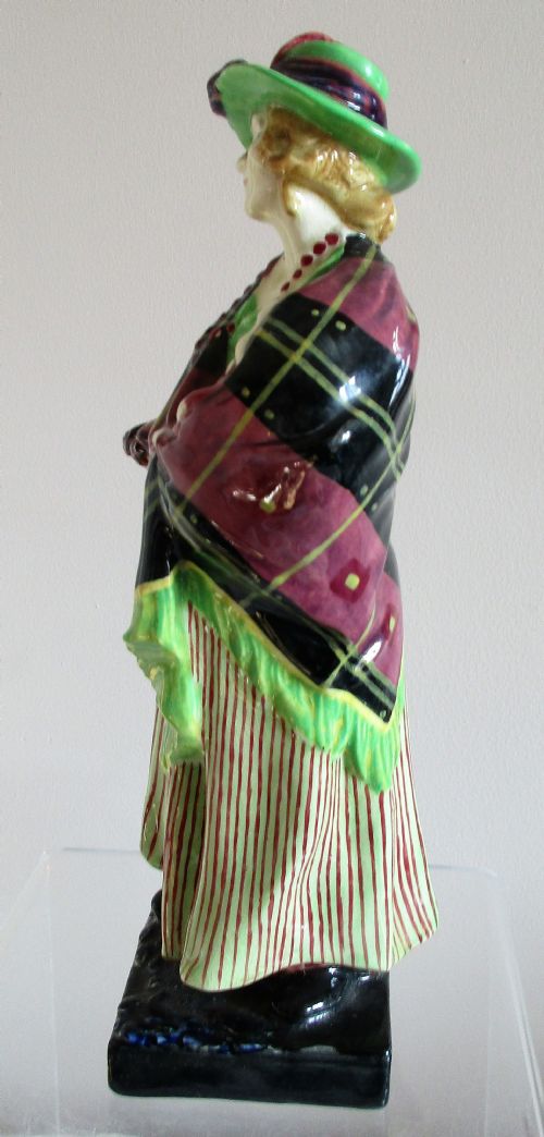 fig 1. A vintage Royal Doulton porcelain figurine depicting a female lavender vendor wearing a green hat, tartan shawl, and striped skirt while carrying a basket of lavender and a child.