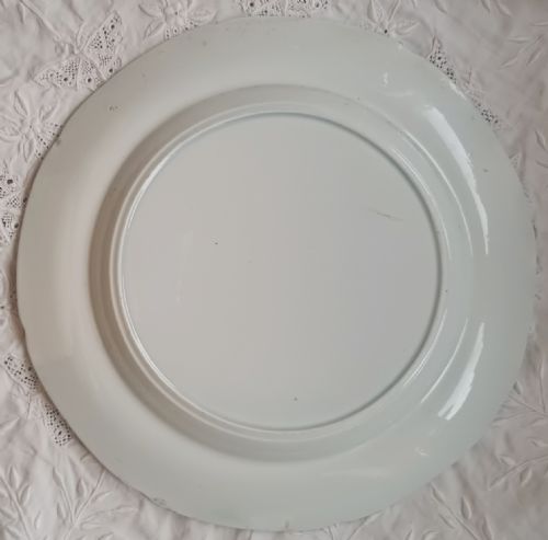 fig 1. A circular blue and white transfer-printed earthenware plate featuring a rural scene with a cottage, cow, and cowman surrounded by a broad floral border.