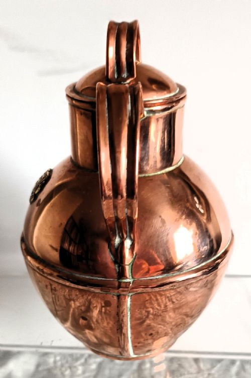 fig 1. A bulbous Victorian polished copper Guernsey milk can featuring a fitted lid, loop handles, and a raised brass Guernsey crest medallion.