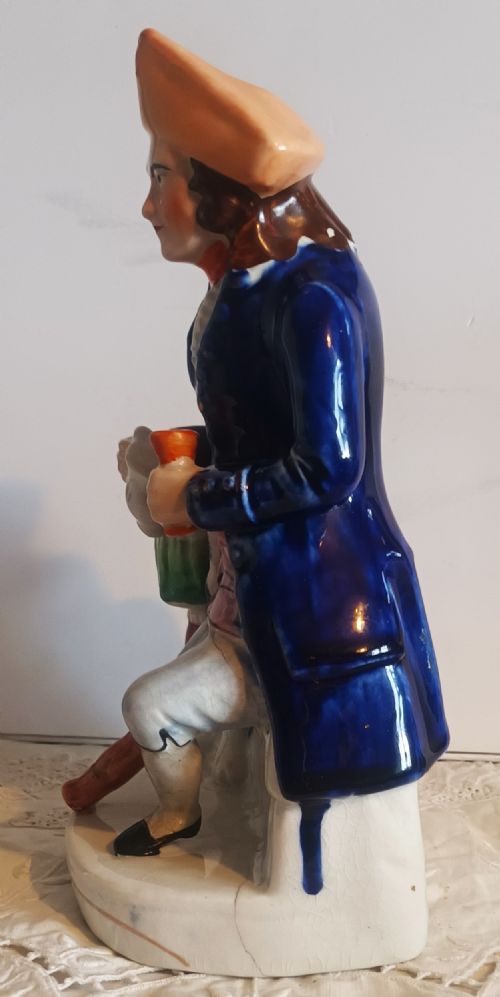 fig 1. A Victorian Staffordshire earthenware ceramic figure depicting a seated sailor with a peg leg wearing a blue coat and tricorn hat.