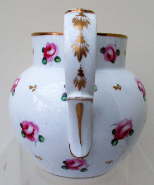 fig 1. An antique white porcelain cream jug featuring hand-painted pink rose sprigs, gold leaf detailing, a pointed sparrow beak spout, and a curved handle.