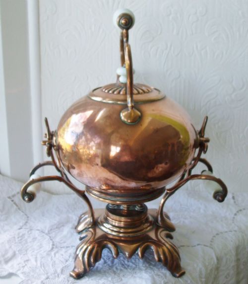 fig 1. An antique Victorian copper spirit kettle featuring a white ceramic handle, gooseneck spout, and decorative brass stand with burner.