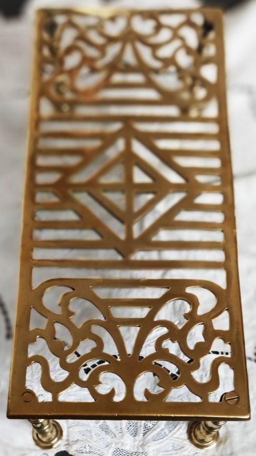 fig 1. A rectangular polished brass trivet featuring openwork geometric and scroll fretwork supported on four turned legs.