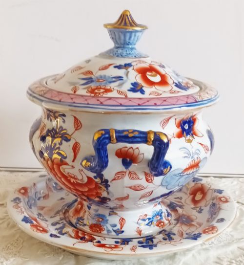 fig 1. An antique Georgian ironstone china soup tureen with a lid and matching stand, decorated in an ornate Japanese Imari style pattern with cobalt blue, rust red, and gilded floral motifs.