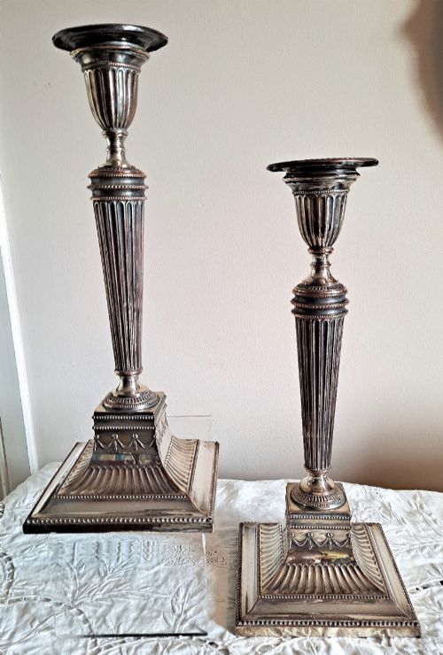 fig 1. A pair of silver-plated Georgian candlesticks featuring fluted shafts, urn sconces, and square decorated bases showing copper wear.