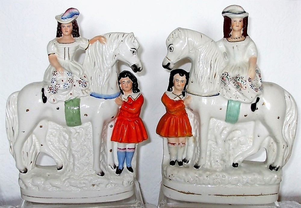 A pair of antique glazed white earthenware figures depicting children in red dresses standing beside white horses on moulded bases.