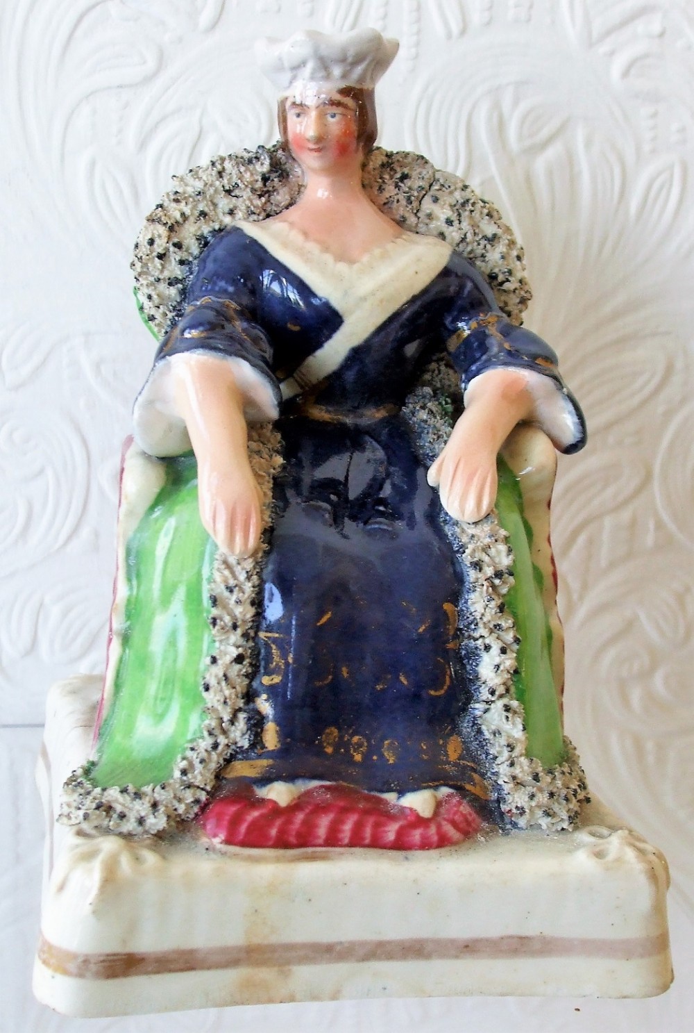 A Victorian Staffordshire earthenware portrait figure depicting Queen Victoria seated on a throne in a cobalt blue dress.