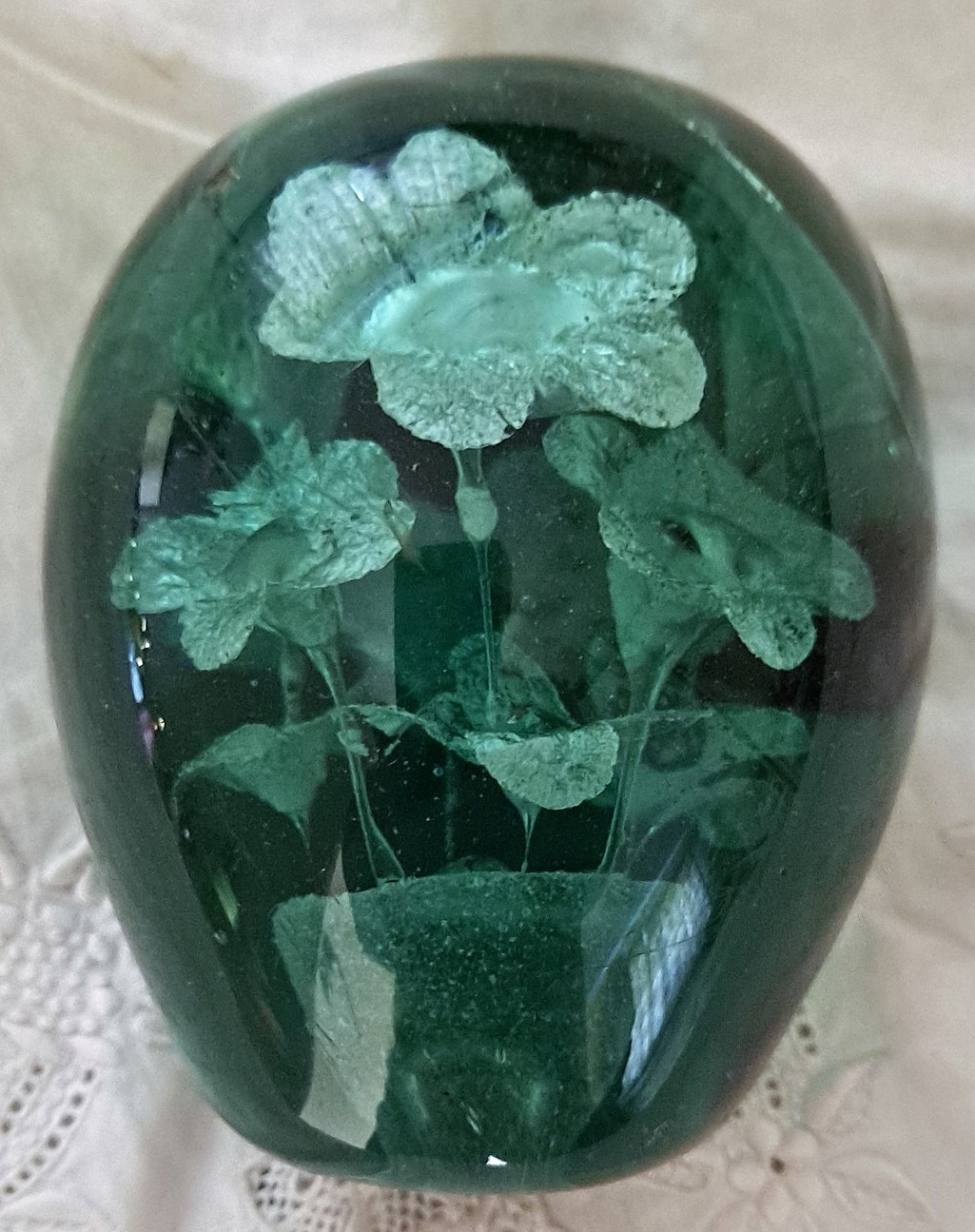 A heavy ovoid dark green glass dump containing an internal encased floral design shaped like a pot of flowers.