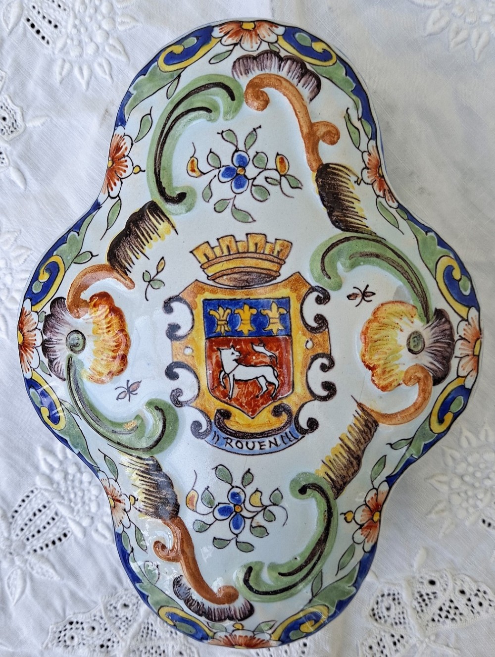 A shaped hand-painted French faience ceramic lidded box featuring polychrome floral scrollwork and a coat of arms inscribed Rouen.
