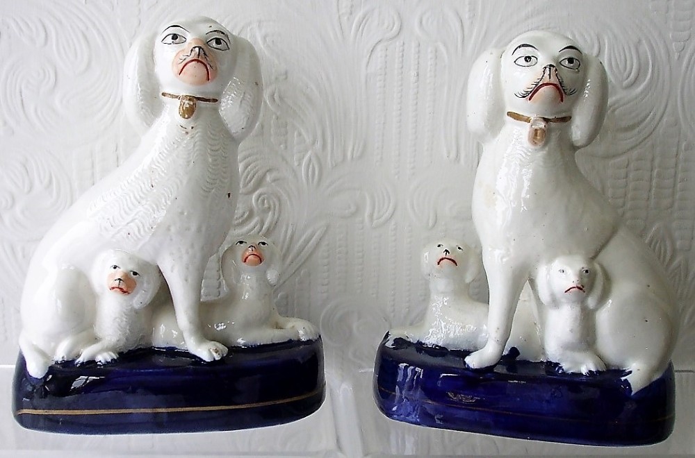 A pair of white glazed earthenware Staffordshire poodle figurines seated on cobalt blue bases with puppies gathered at their feet.