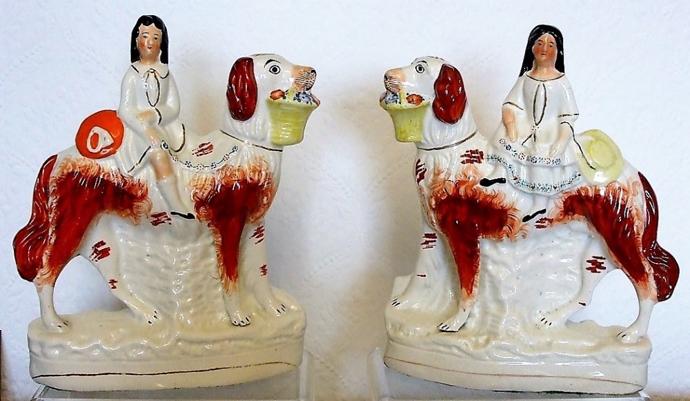 A facing pair of Victorian Staffordshire earthenware figures depicting children riding rust and white setter dogs carrying baskets of flowers.