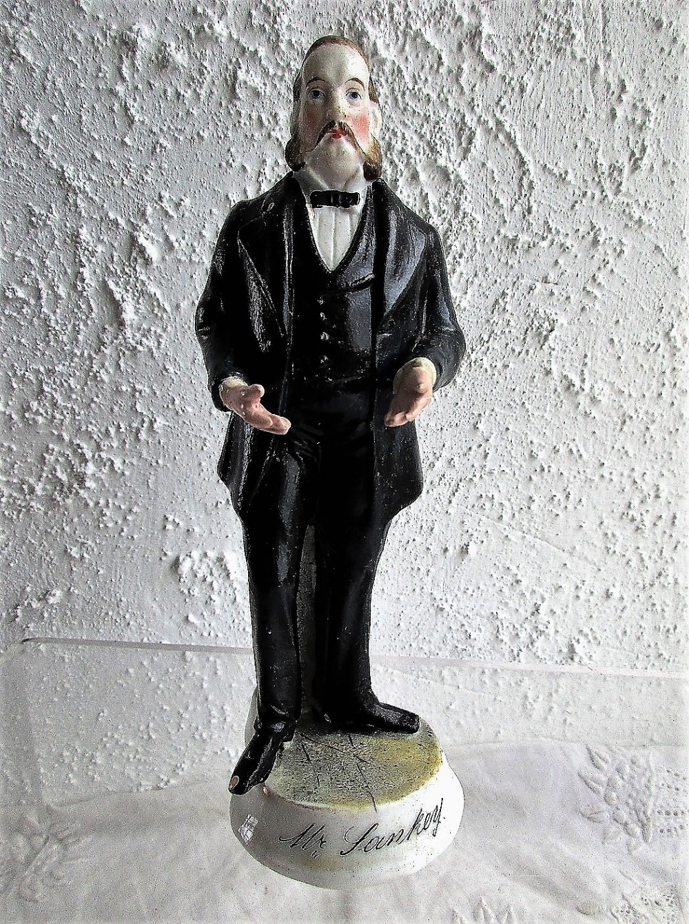 A standing Victorian porcelain figurine of a man wearing a black frock coat with outstretched hands, mounted on a round base inscribed with Mr Sankey.