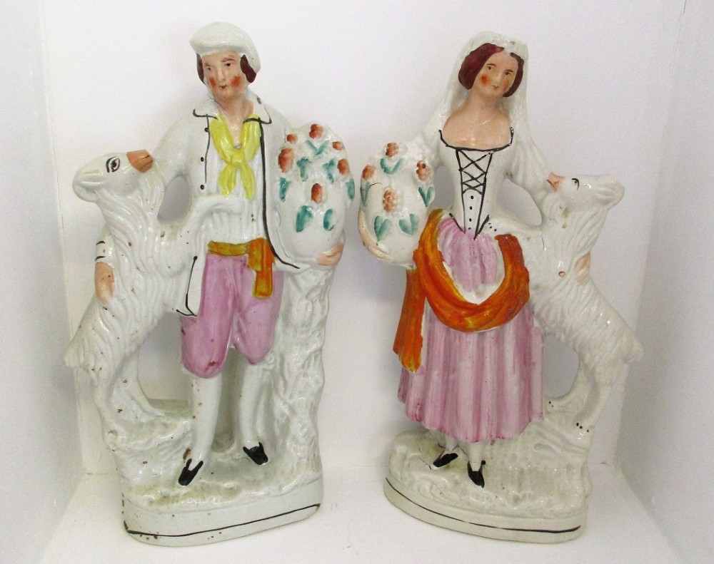 A pair of antique Victorian Staffordshire earthenware figures depicting a male and female goatherd with goats and baskets of flowers.