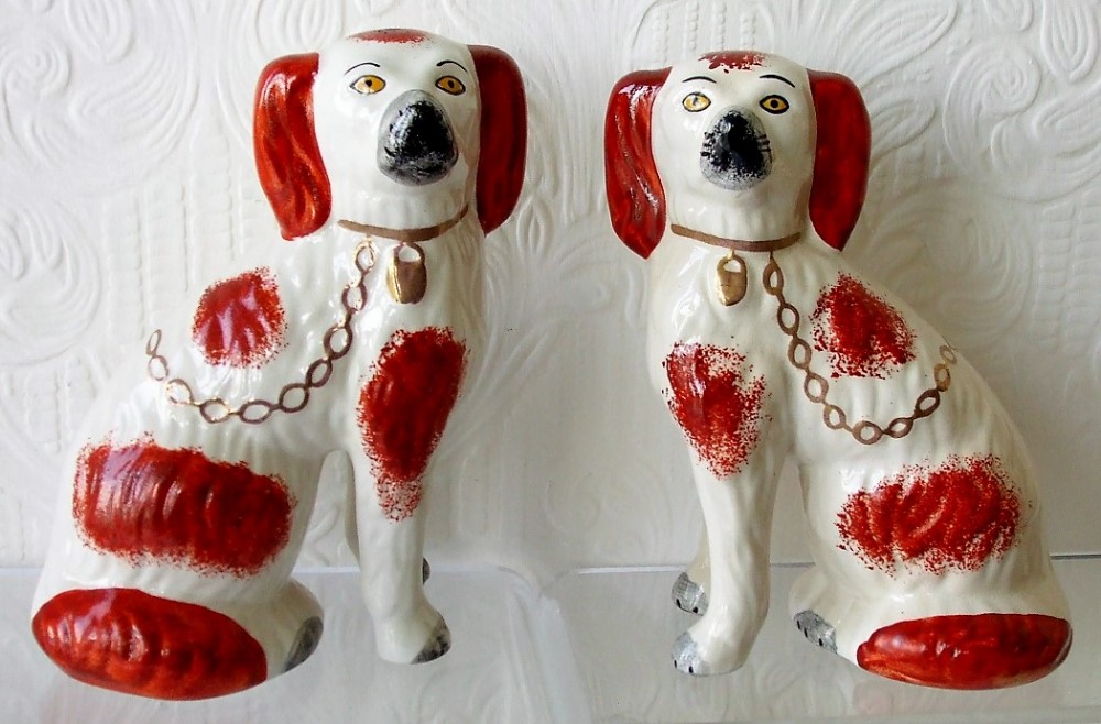 A pair of seated Victorian Staffordshire earthenware spaniel figurines painted white with russet patches, black snouts, and gold collars with chains.