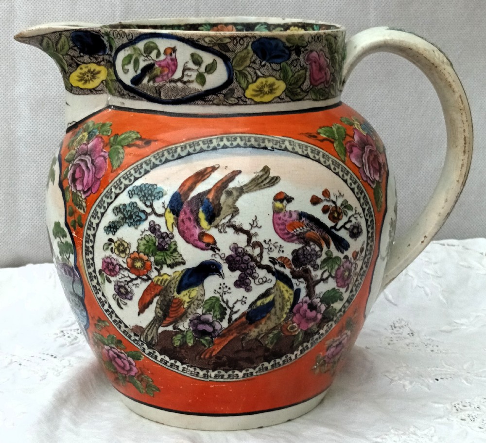 An antique Georgian pearlware Dutch jug featuring a bright orange ground and decorative oval medallions depicting hand-painted polychrome birds and foliage.
