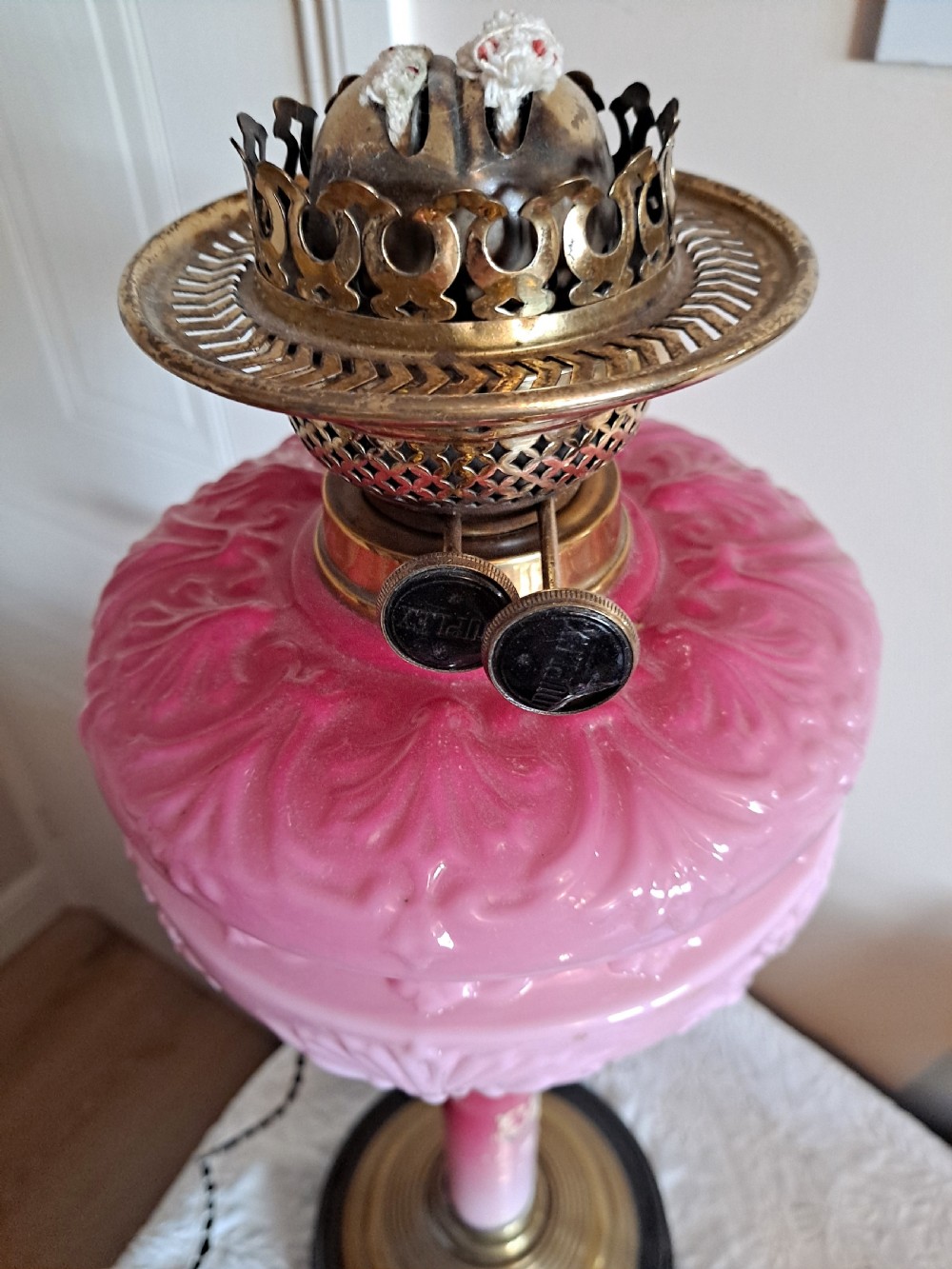 A Victorian column oil lamp featuring a cranberry pink etched glass shade, a matching pink glass reservoir, and a brass column on a black circular base. View X