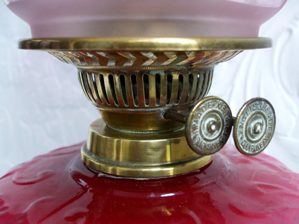 A Victorian oil lamp with a cast brass scrolled base, a pink moulded glass font, and a cranberry frilled glass shade. View IV
