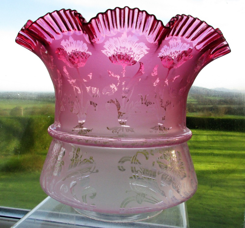 A Victorian oil lamp with a cast brass scrolled base, a pink moulded glass font, and a cranberry frilled glass shade. View V