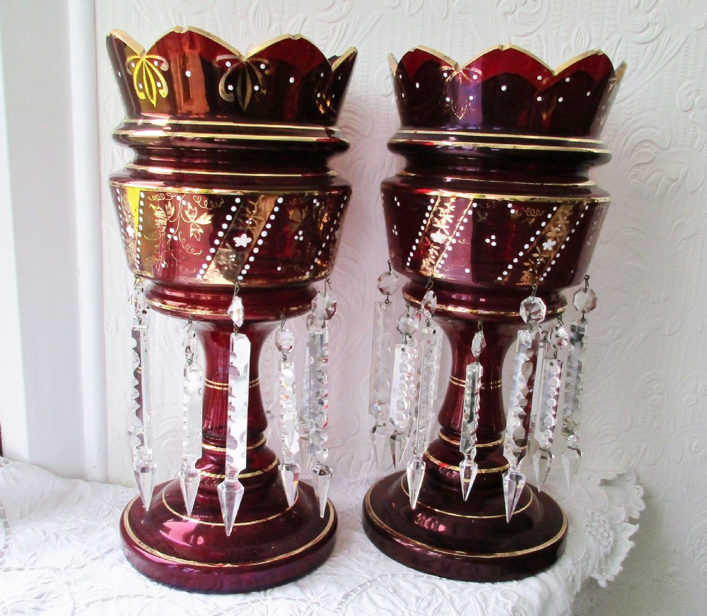 A pair of deep ruby red glass Victorian lustres featuring scalloped upper rims, hand-painted gold foliage, and suspended clear cut-crystal prisms.