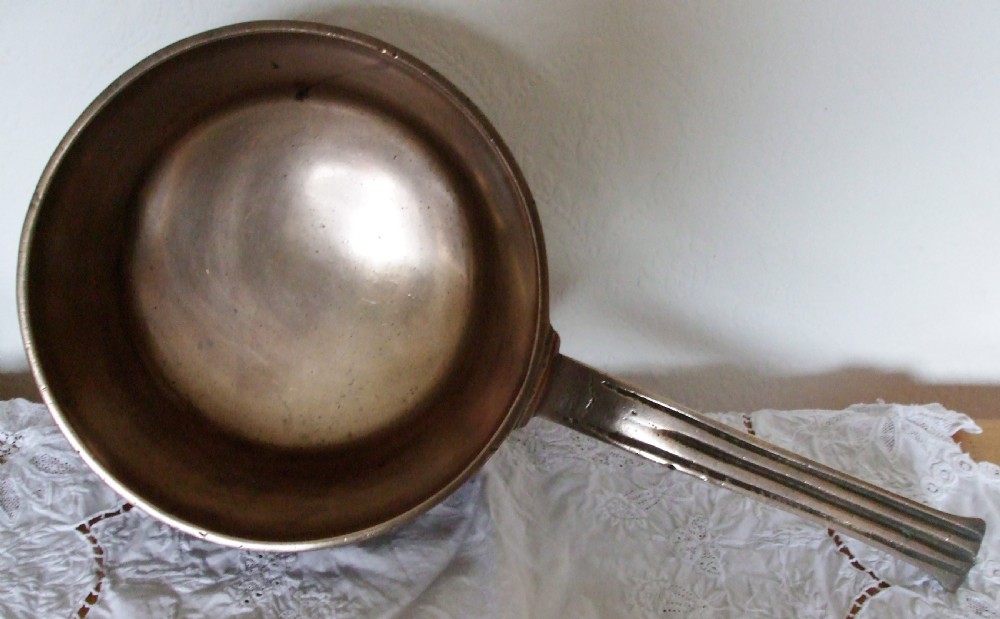 An antique Georgian cast bronze posnet skillet featuring three short tripod legs, a polished metal interior, and a long flat handle. View II