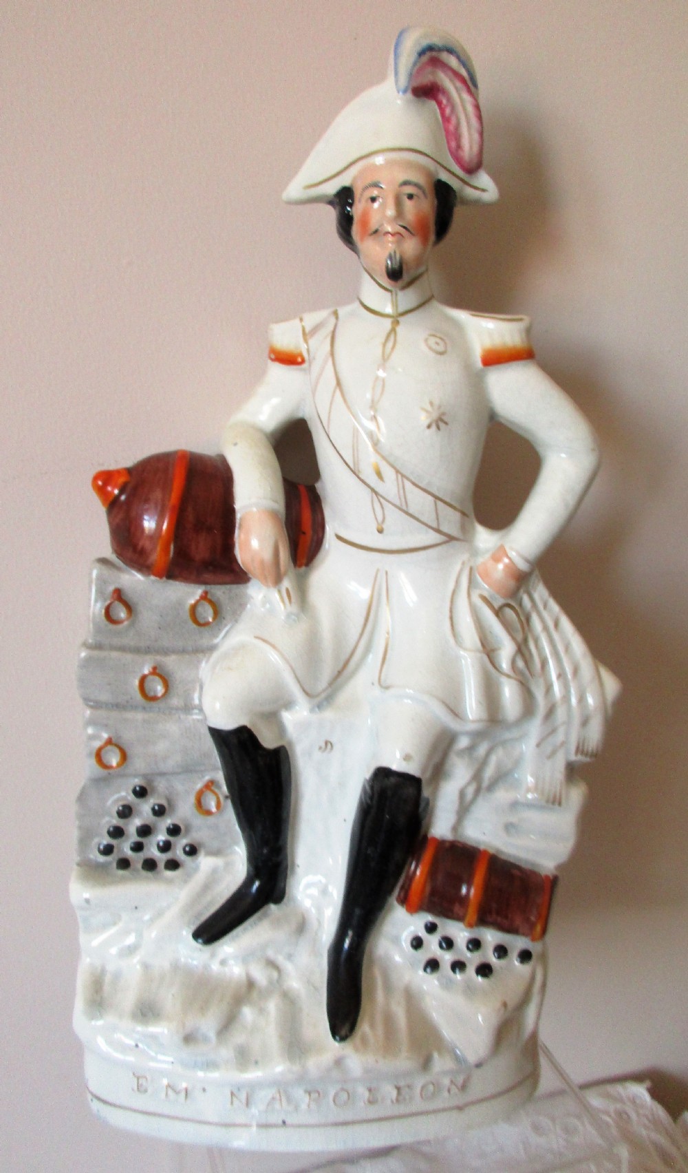 An antique Victorian Staffordshire earthenware portrait figure depicting Emperor Napoleon III in uniform seated beside a cannon.