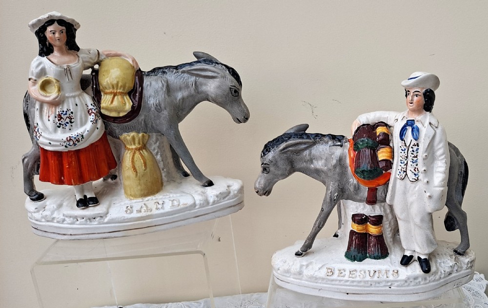 Pair of Victorian Staffordshire earthenware pottery figures depicting a woman and a man standing next to pack donkeys labelled Sand and Beesums.