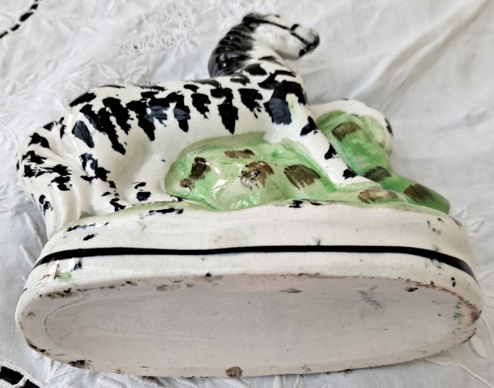 A Victorian Staffordshire earthenware zebra figurine hand-painted with black stripes on a white body, standing on a green molded base. View V