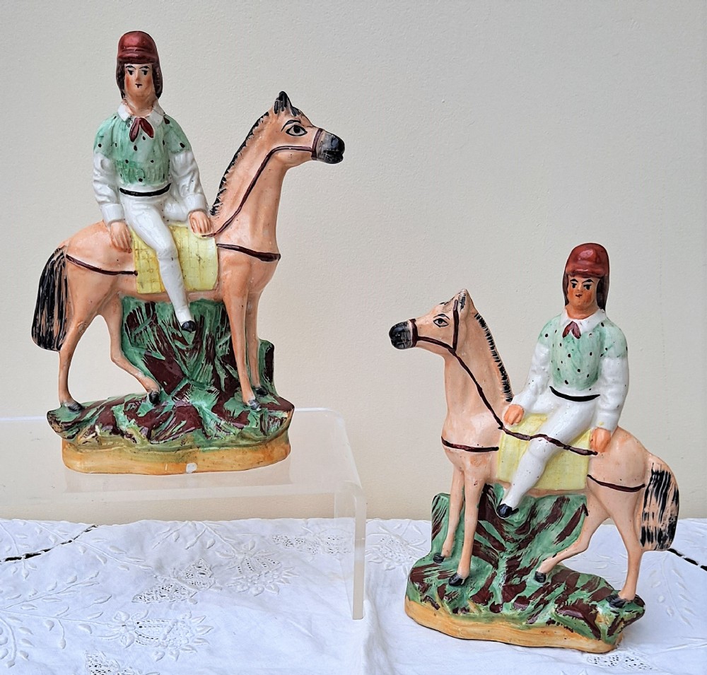 A pair of antique Victorian Staffordshire ceramic figures depicting jockeys in green spotted jackets mounted on tan horses.