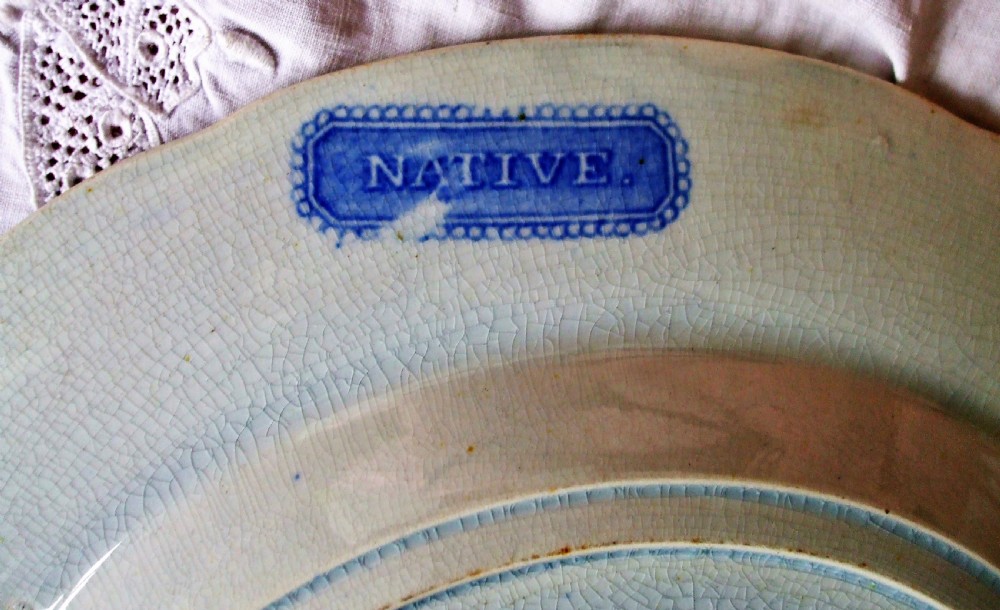 An antique Georgian circular earthenware plate featuring a cobalt blue and white transfer printed landscape with figures and horses near a cottage, surrounded by a floral border. View III
