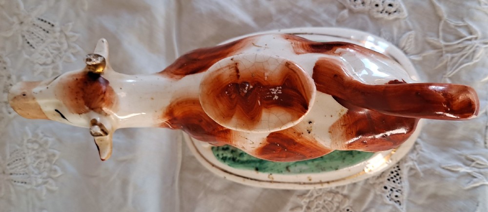 A pair of antique Victorian Staffordshire earthenware cow creamers with reddish-brown painted patches standing on green molded oval bases. View VI
