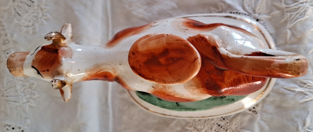 A pair of antique Victorian Staffordshire earthenware cow creamers with reddish-brown painted patches standing on green molded oval bases. View XII