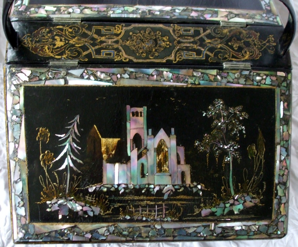 A Victorian black lacquered papier-mache needlework casket featuring mother-of-pearl inlay, gilded foliate patterns, and an overhead carrying handle. View IV