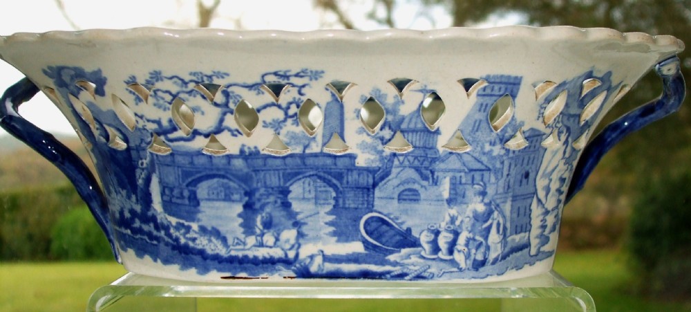 An antique oval blue and white earthenware chestnut basket featuring pierced openwork sides and a central printed river landscape scene. View IV