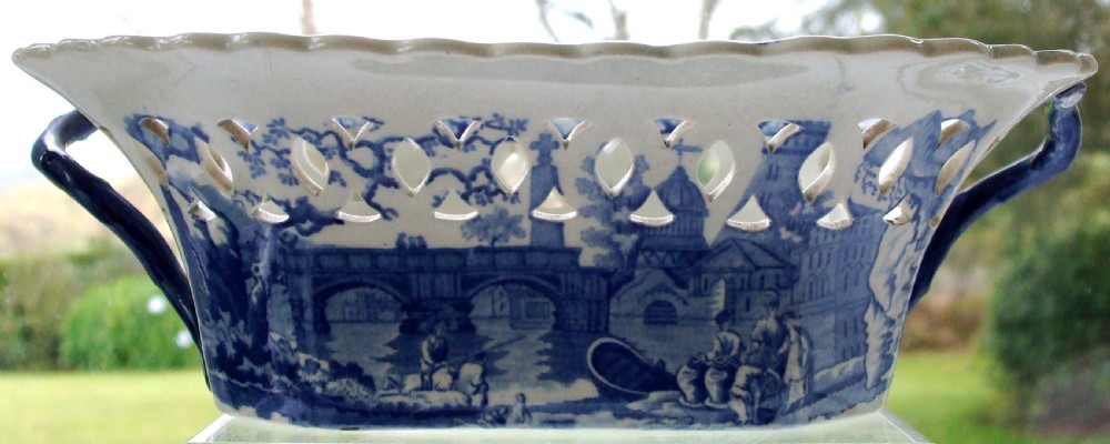 An antique oval blue and white earthenware chestnut basket featuring pierced openwork sides and a central printed river landscape scene. View VI