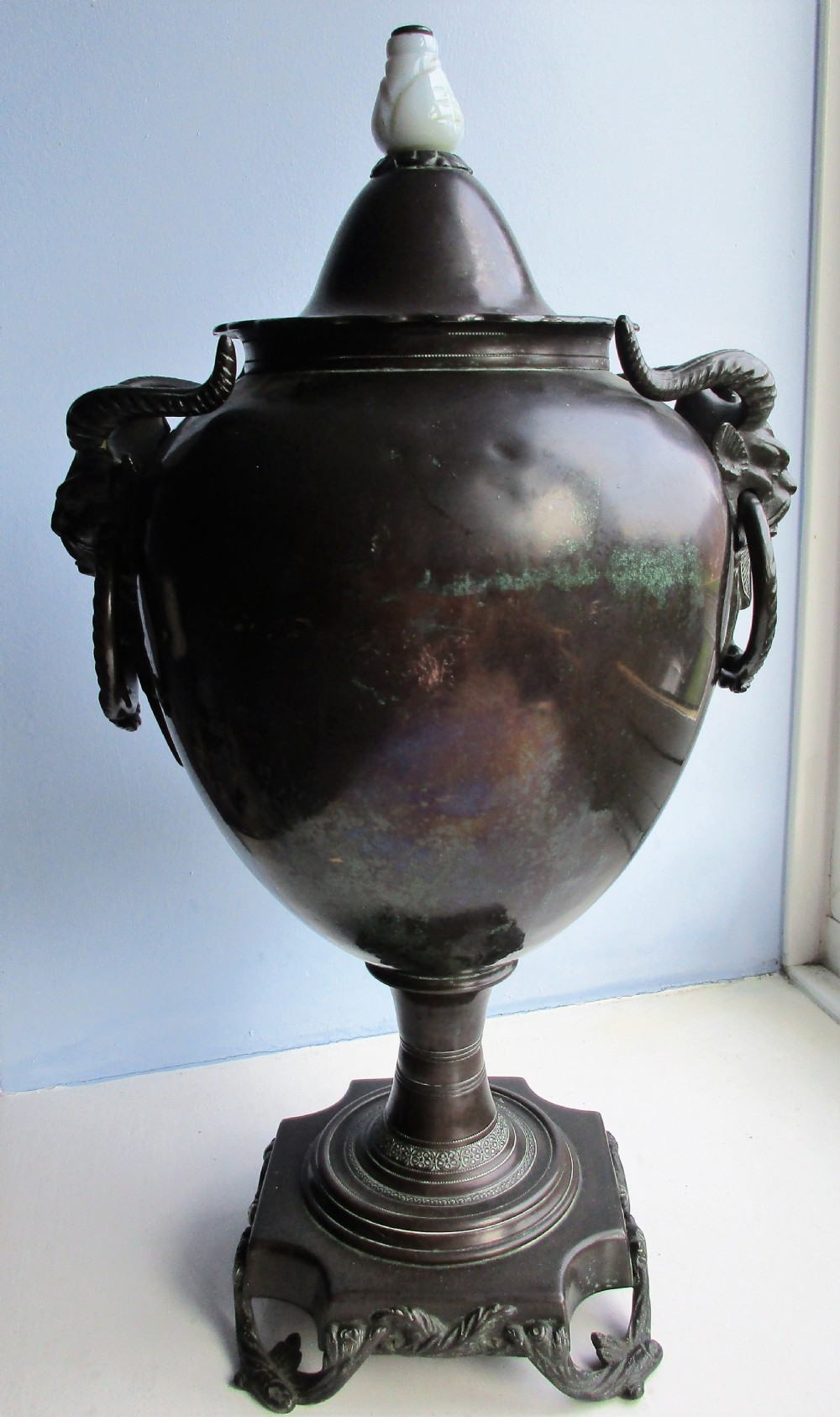 An antique Victorian japanned dark metal tea urn featuring a tapered body, ornate cast side handles, a front spigot, and a white top finial. View III