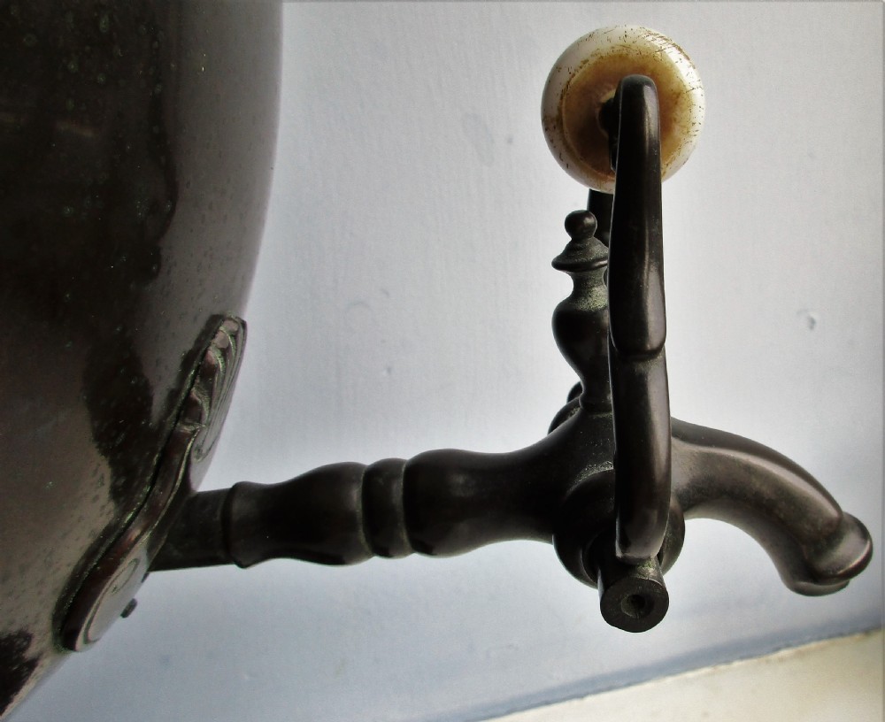 An antique Victorian japanned dark metal tea urn featuring a tapered body, ornate cast side handles, a front spigot, and a white top finial. View VI