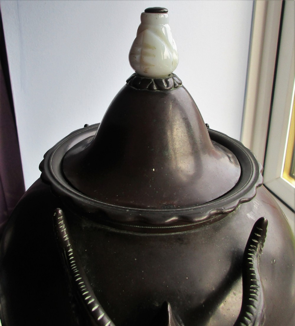 An antique Victorian japanned dark metal tea urn featuring a tapered body, ornate cast side handles, a front spigot, and a white top finial. View VIII