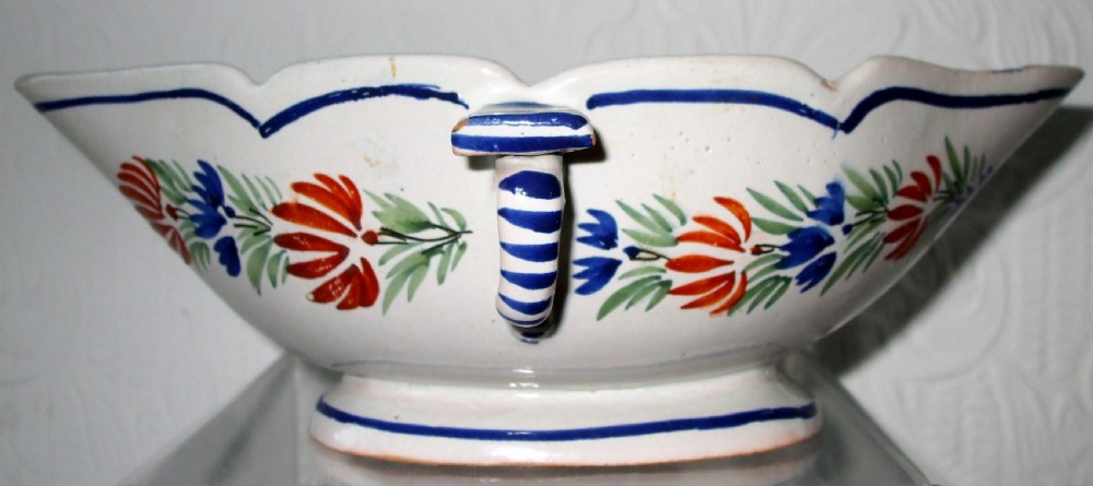 An off-white tin-glazed earthenware double sauceboat featuring hand-painted red and blue botanical decorations and a scalloped blue rim. View III