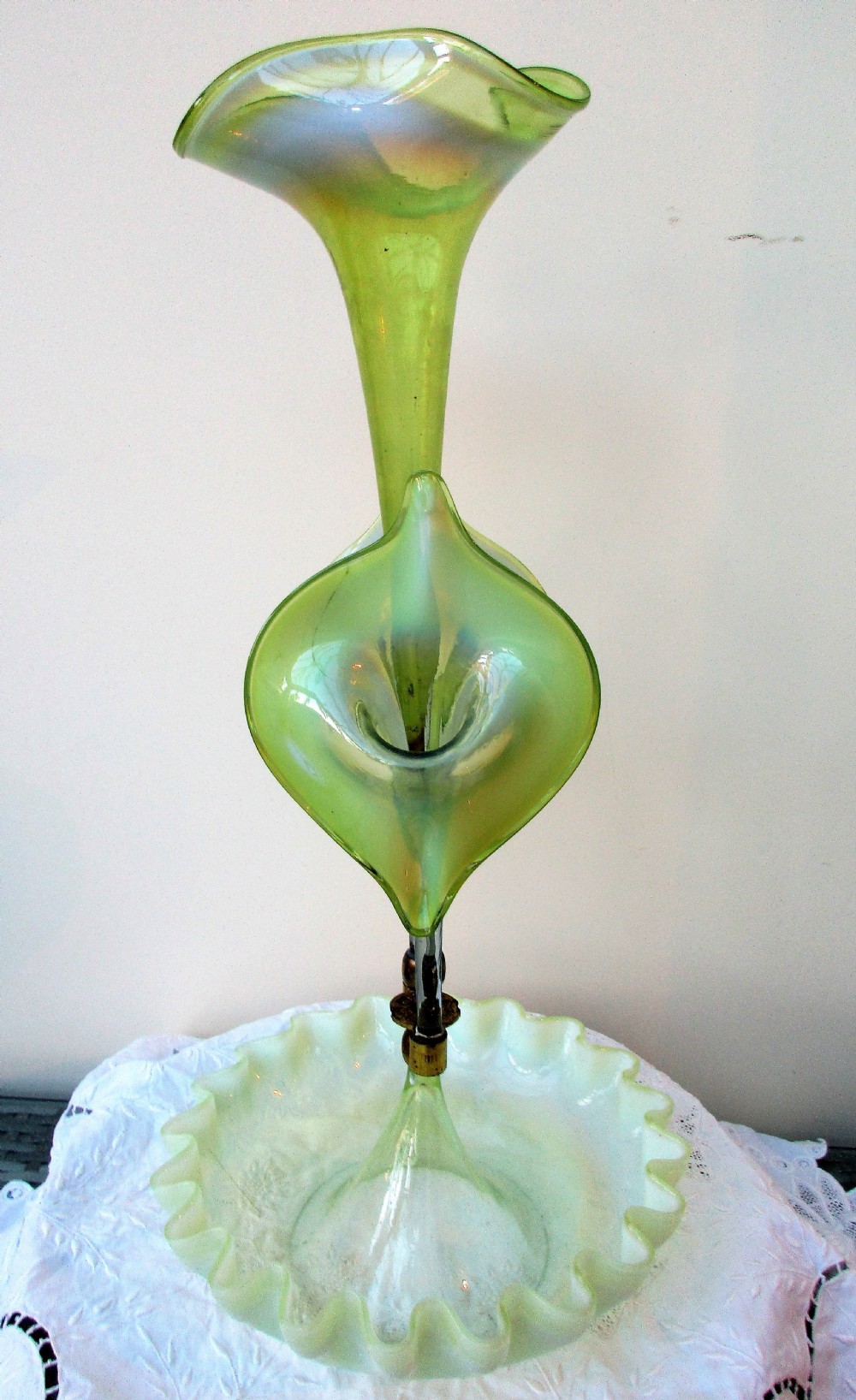 A Victorian Art Nouveau translucent green glass epergne featuring a ruffled base bowl and two fluted lily-form glass trumpets joined by a metal collar.