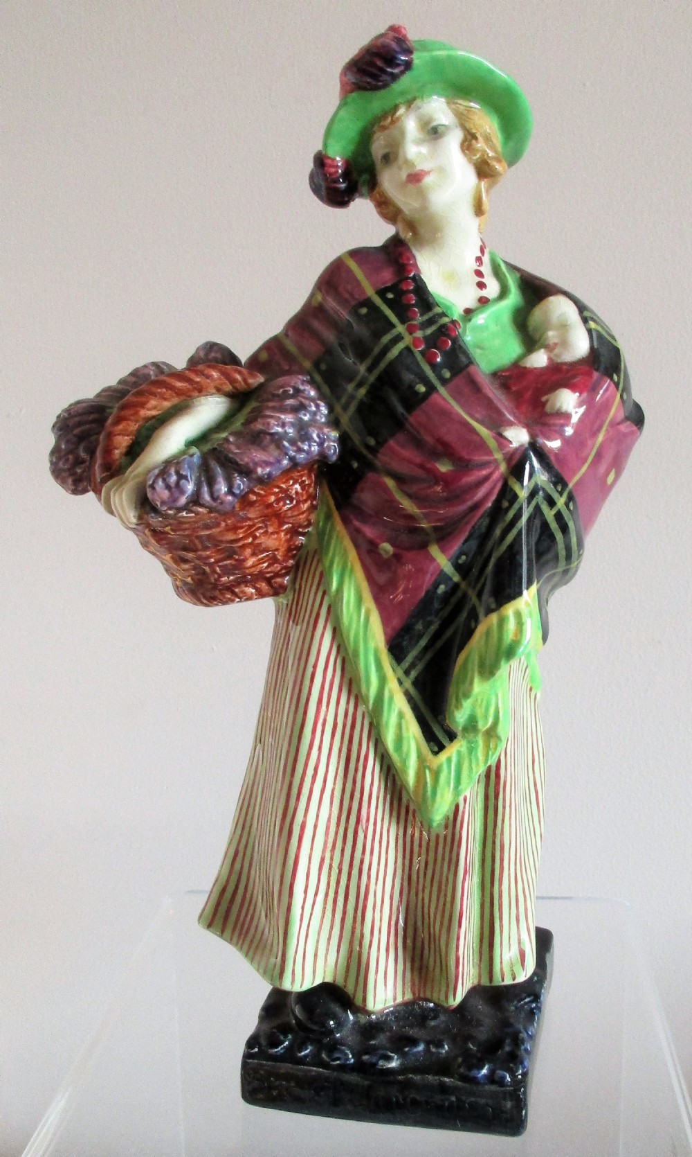 A vintage Royal Doulton porcelain figurine depicting a female lavender vendor wearing a green hat, tartan shawl, and striped skirt while carrying a basket of lavender and a child.