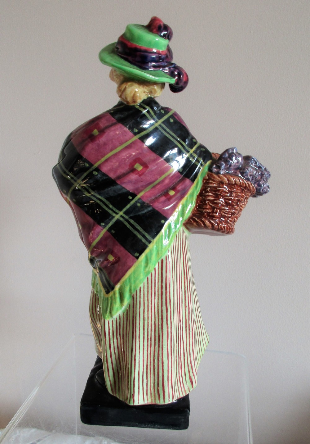 A vintage Royal Doulton porcelain figurine depicting a female lavender vendor wearing a green hat, tartan shawl, and striped skirt while carrying a basket of lavender and a child. View III