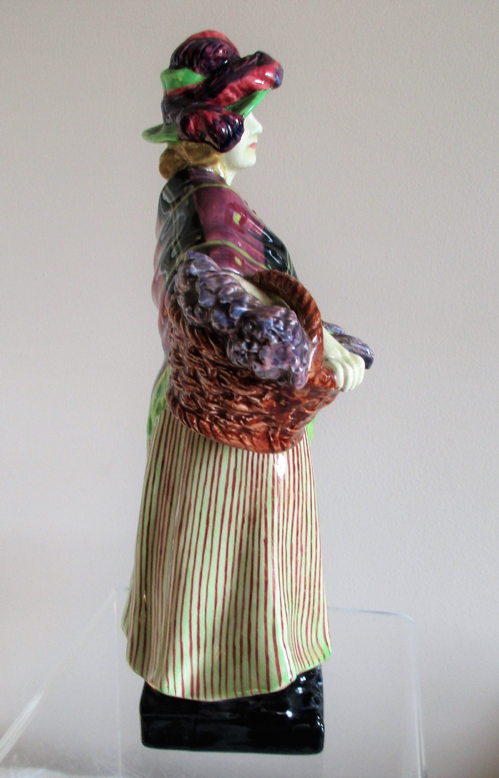 A vintage Royal Doulton porcelain figurine depicting a female lavender vendor wearing a green hat, tartan shawl, and striped skirt while carrying a basket of lavender and a child. View IV