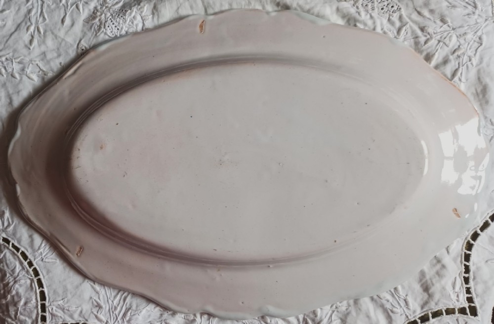 An oval tin-glazed ceramic platter featuring a hand-painted Breton woman surrounded by floral borders and the inscription Pornic. View II