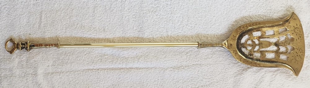 A three-piece set of Victorian brass fire irons comprising a poker, a shovel with a pierced scroll blade, and a pair of decorative tongs. View II