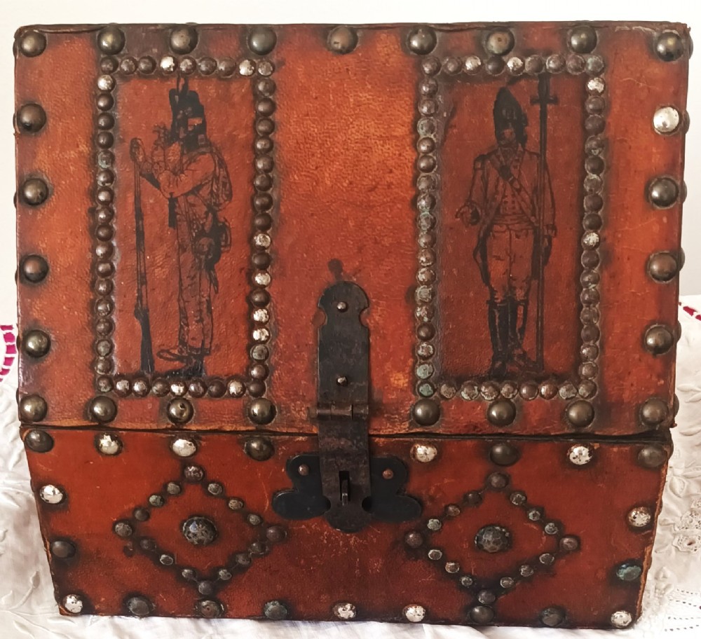 A rectangular Georgian leather-bound casket decorated with brass studs, etched military figure illustrations, and a central iron latch.