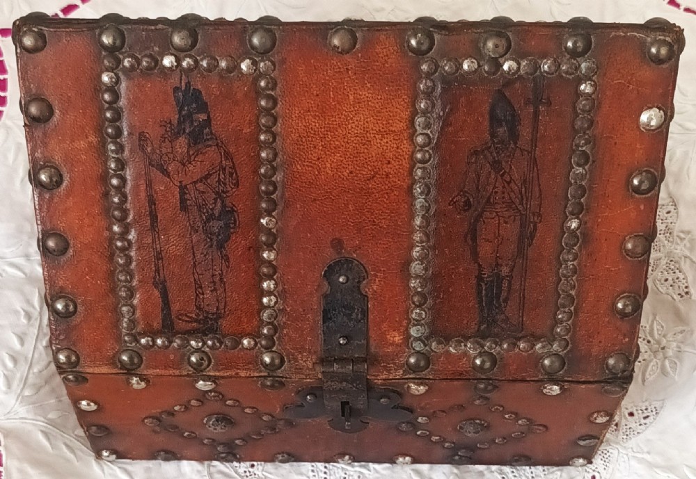 A rectangular Georgian leather-bound casket decorated with brass studs, etched military figure illustrations, and a central iron latch. View II