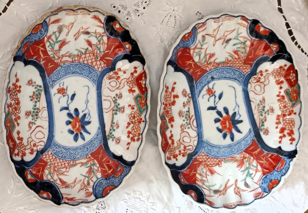 A pair of oval antique Japanese Imari porcelain dishes with scalloped rims, featuring hand-painted floral and bird motifs in cobalt blue, iron red, and white enamels.