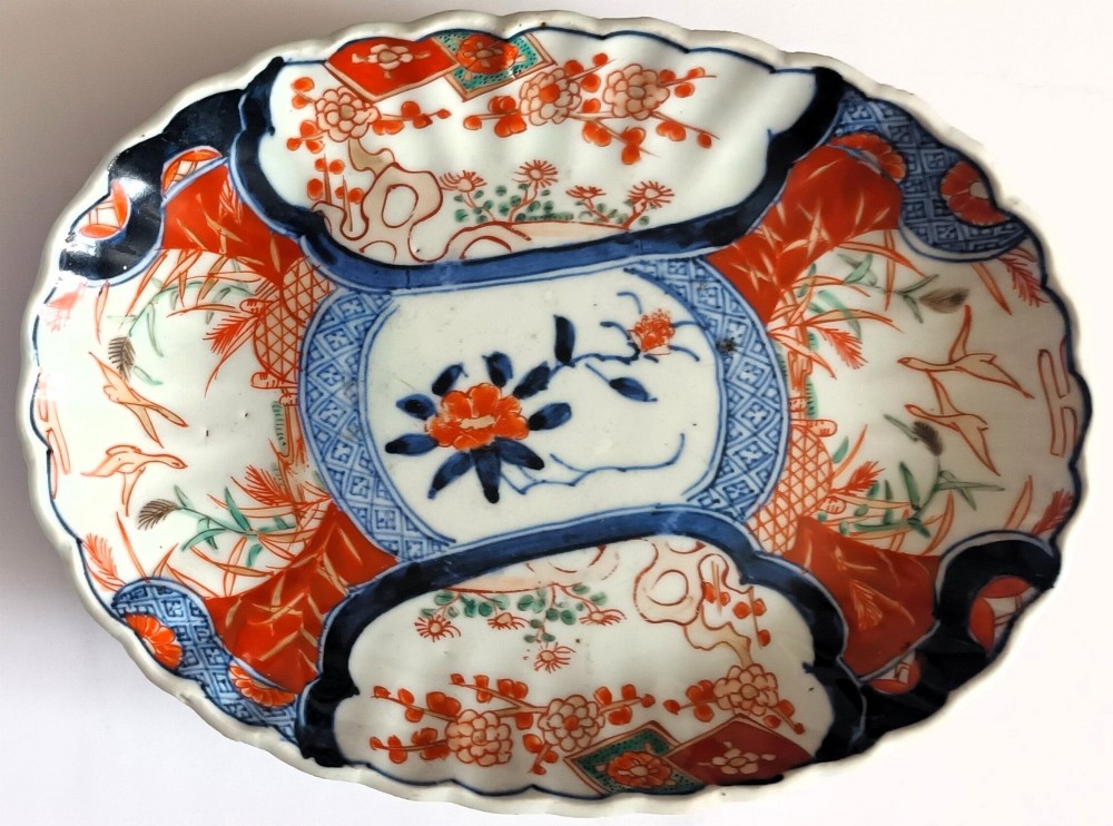 A pair of oval antique Japanese Imari porcelain dishes with scalloped rims, featuring hand-painted floral and bird motifs in cobalt blue, iron red, and white enamels. View V