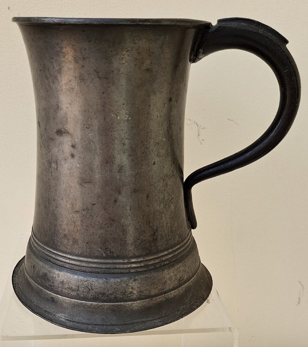 An antique Victorian pewter quart mug featuring a concave waist, flared base with moulded trim, and a dark curved loop handle.